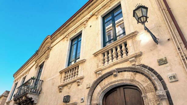 A historic building with a large wooden door, ornate balconies, and a classic street lamp. - Varò Apartment (Taormina)