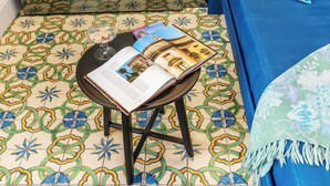 A room with a patterned floor, a small table with a book and a glass, and a blue sofa. - Varò Apartment (Taormina)