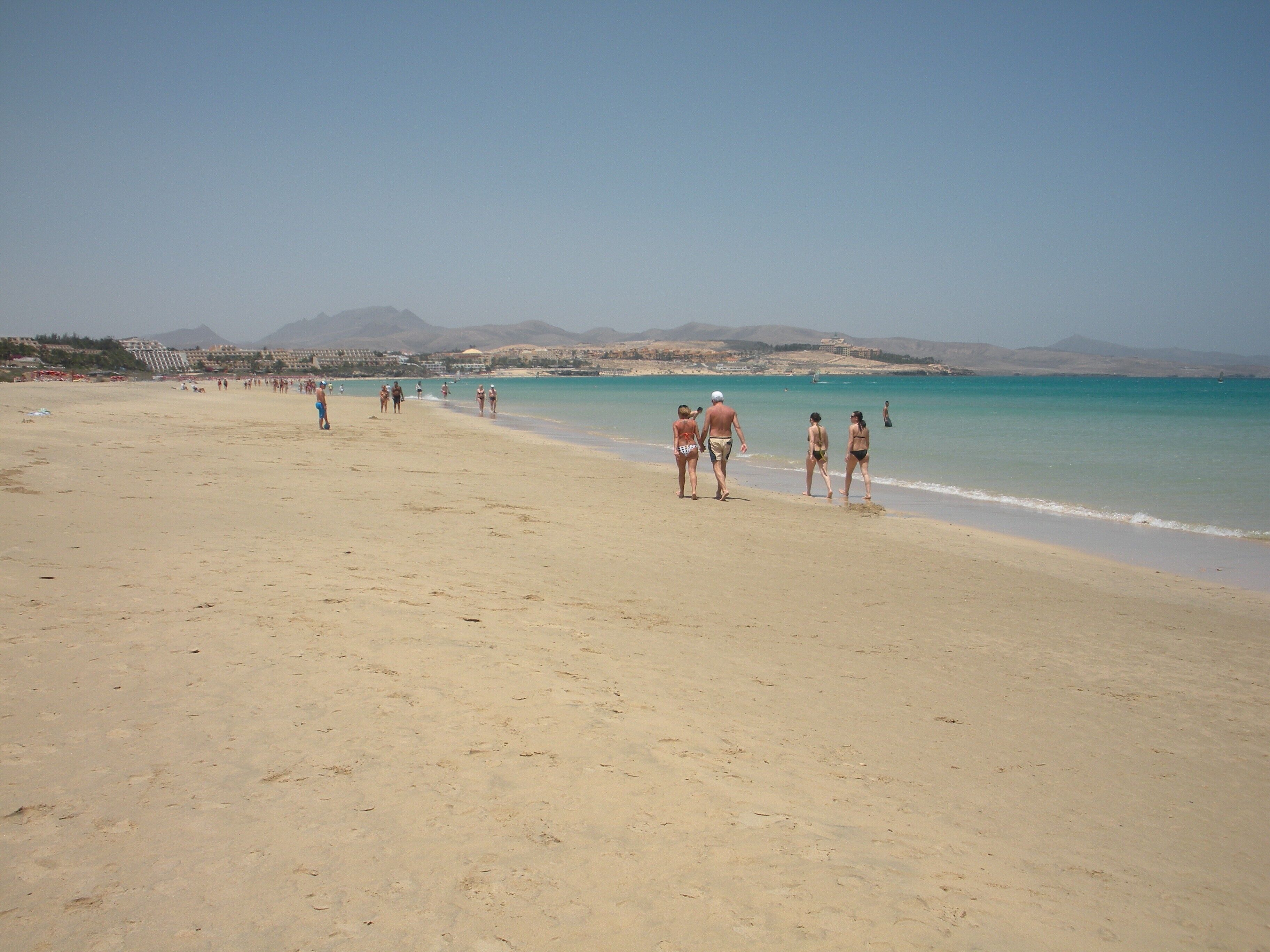 A beach with people walking along the shore and a clear sky.