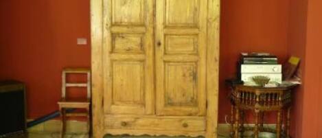 A wooden wardrobe with two doors, a small table with books, and a chair in a room with red walls.