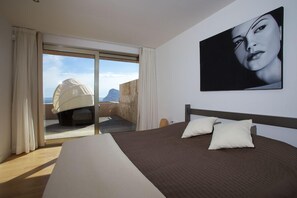 Un dormitorio con una cama grande, vistas al mar a través de una puerta corredera y un cuadro en la pared.