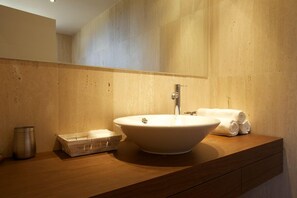 Un baño moderno con un lavamanos ovalado grande, un espejo y un mueble de tocador de madera.