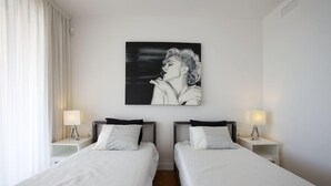Una habitación de hotel con dos camas individuales, ropa de cama blanca y una obra de arte colgada en la pared que muestra a una mujer.