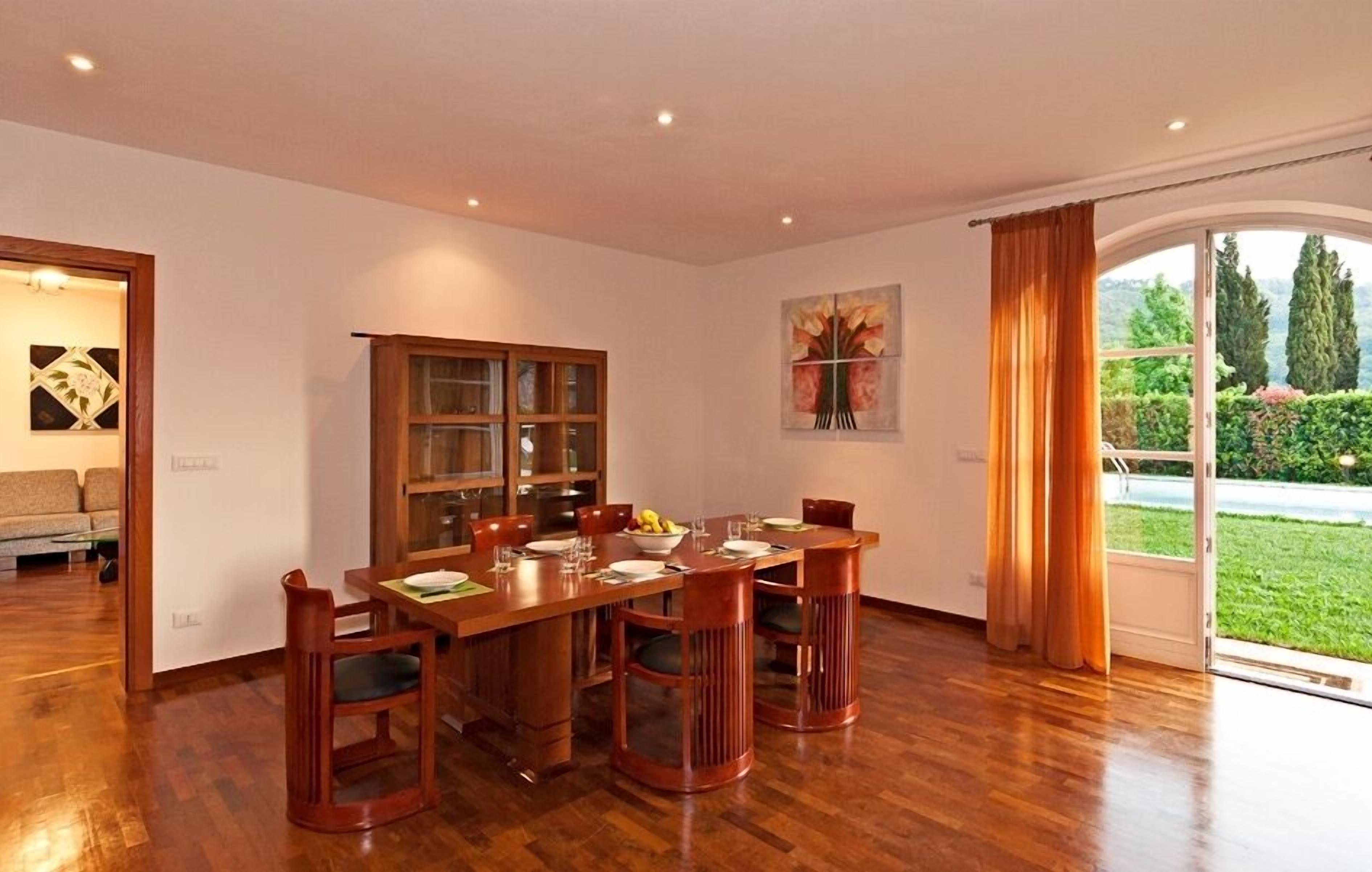 A dining area with a wooden table and chairs, a glass cabinet, and a painting on the wall.