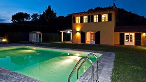 A two-story house with a swimming pool, a small shed, and a well-lit exterior at dusk. -  Very beautiful Villa / Private Swimming Pool / PrivateGarden / Jacuzzi (Lucca)