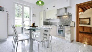 A modern kitchen with white cabinets, a granite countertop, and stainless steel appliances. There is a dining area with a glass table and white chairs. -  Very beautiful Villa / Private Swimming Pool / PrivateGarden / Jacuzzi (Lucca)