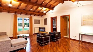 A living room with wooden flooring, a sofa, two black ottomans, a glass coffee table, a television, and a door leading to another room. -  Very beautiful Villa / Private Swimming Pool / PrivateGarden / Jacuzzi (Lucca)