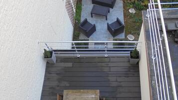 Een dakterras met een houten tafel en bankjes, omgeven door een witte muur en een houten hek.