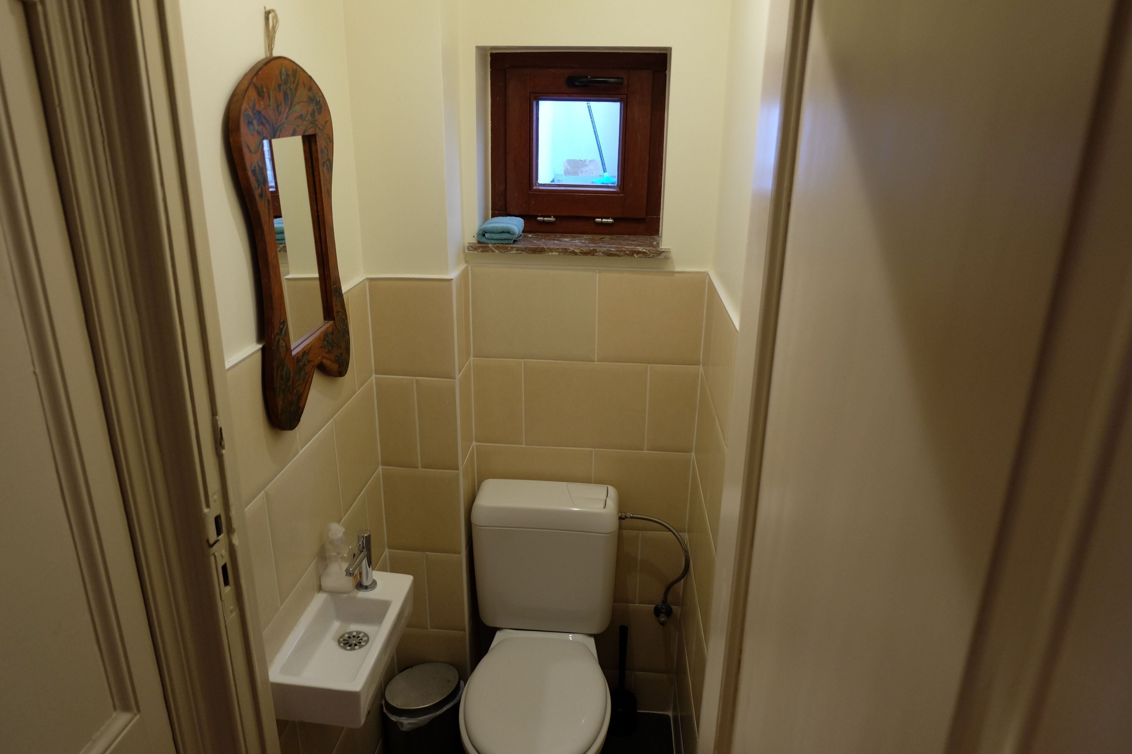 Un baño pequeño con inodoro, lavamanos y una ventana sobre el inodoro.