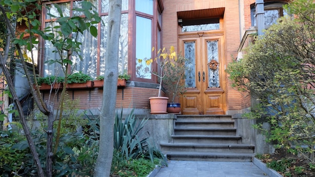 A building with a wooden front door, steps leading up to it, and potted plants around the entrance.