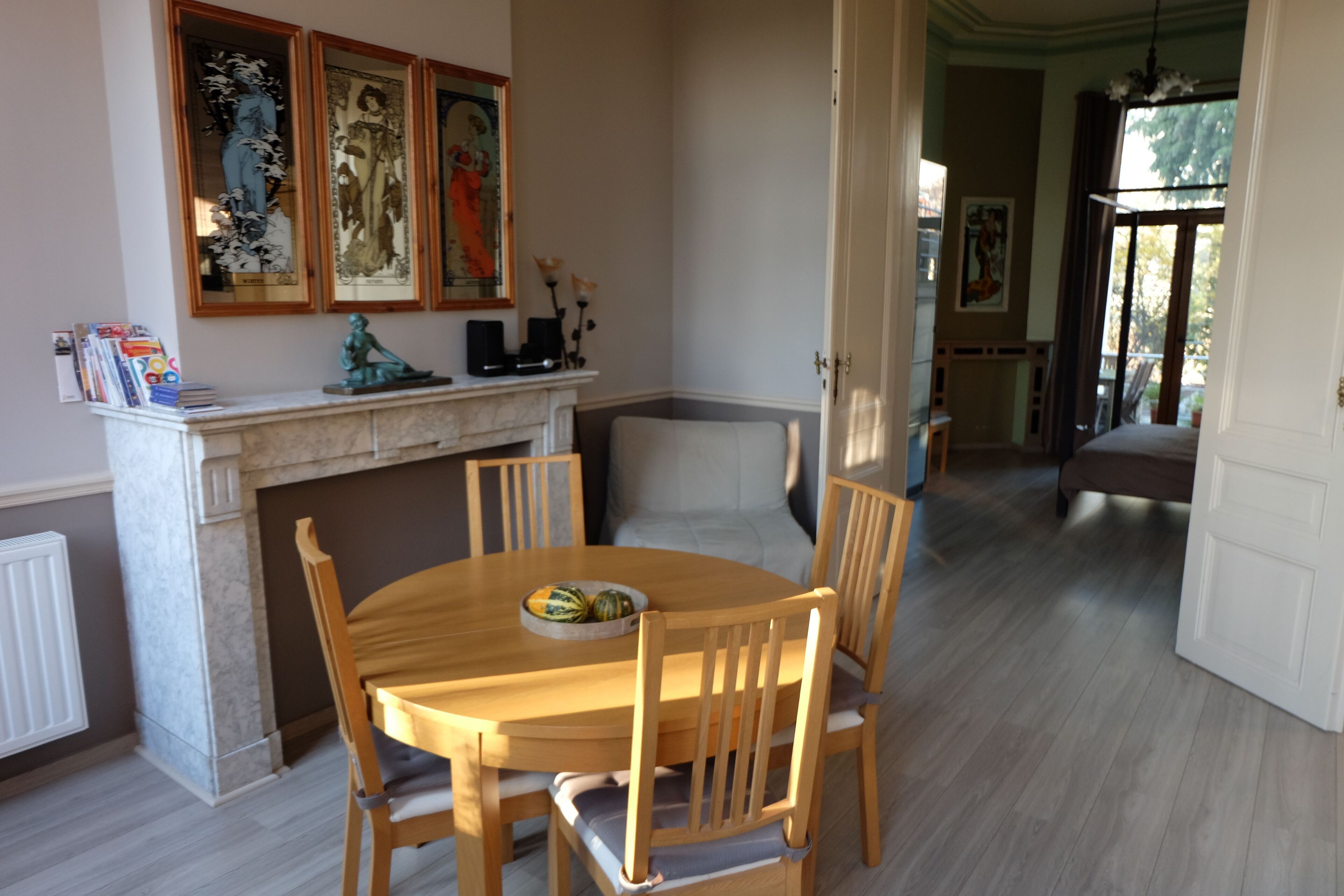 Un comedor con una mesa de madera redonda, cuatro sillas, una chimenea de mármol y cuadros en la pared.