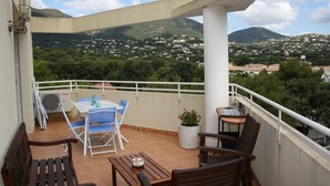 Un balcon avec une table, des chaises et un banc. On y trouve une plante en pot et un ordinateur portable.