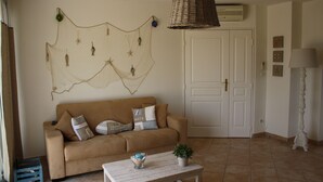 Un salon avec un canapé beige, une table basse, un filet décoratif accroché au mur et une lampe.