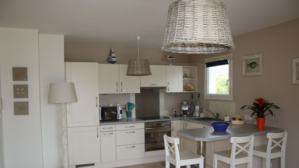 Une cuisine moderne avec des meubles blancs, un îlot central doté de tabourets, un luminaire suspendu et une fenêtre offrant une belle vue.
