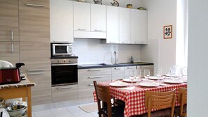 A modern kitchen with white cabinets, a microwave, and a stove. There is a dining table with a red and white checkered tablecloth and chairs. - Villa, private pool,mountain views. Aircon included in price. Visit cinqueterre! (Vigneta)