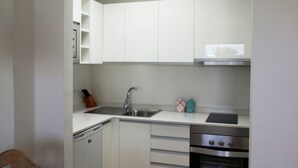 A compact kitchen with white cabinets, a stainless steel sink, a dishwasher, and an oven. - Thomas Beach House Costa Teguise (Costa Teguise)