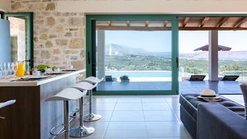 A modern kitchen with a stone wall, a bar area with stools, and a view of the mountains and sea through large glass doors.