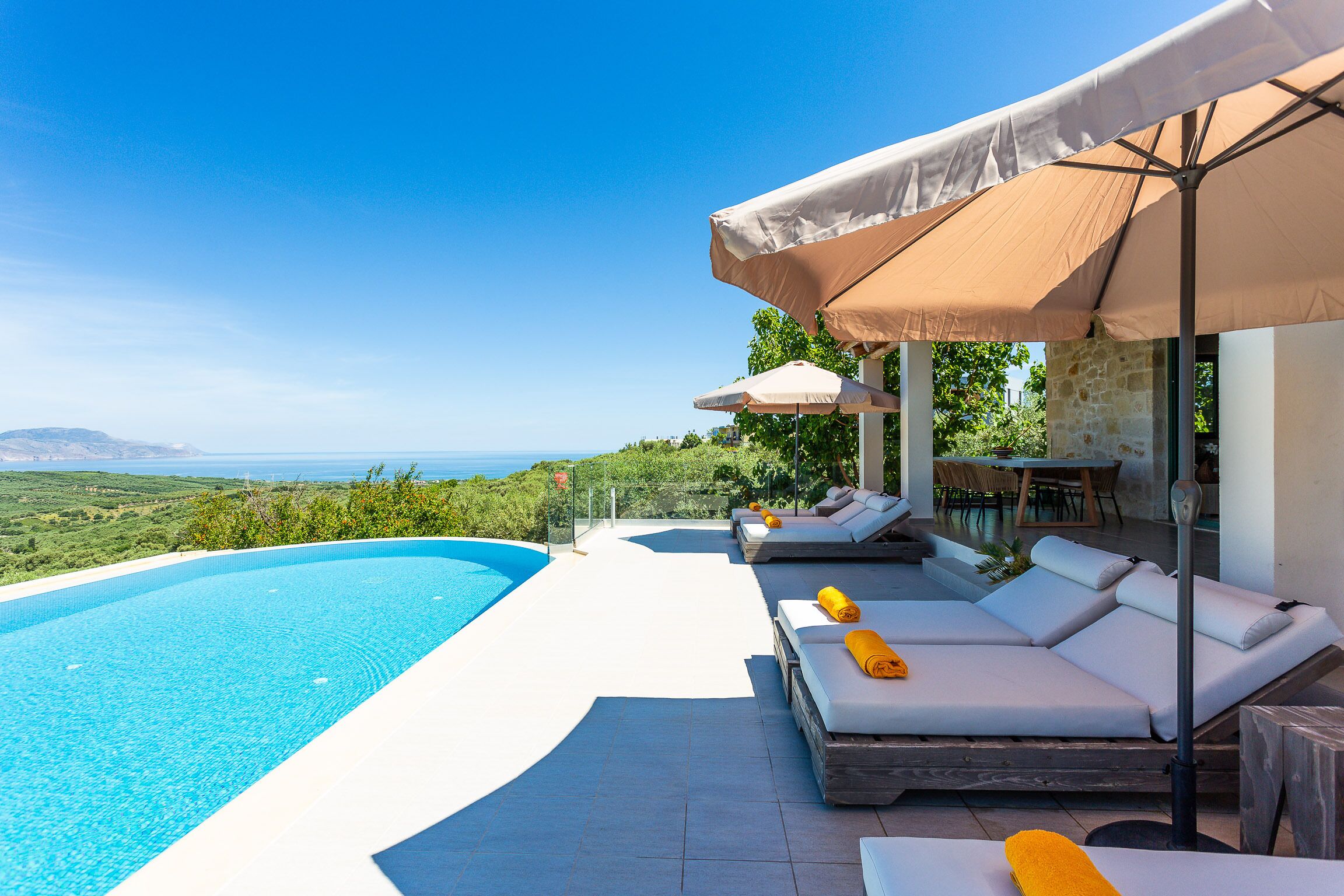 A poolside area with a view of the sea, sun loungers, and umbrellas.