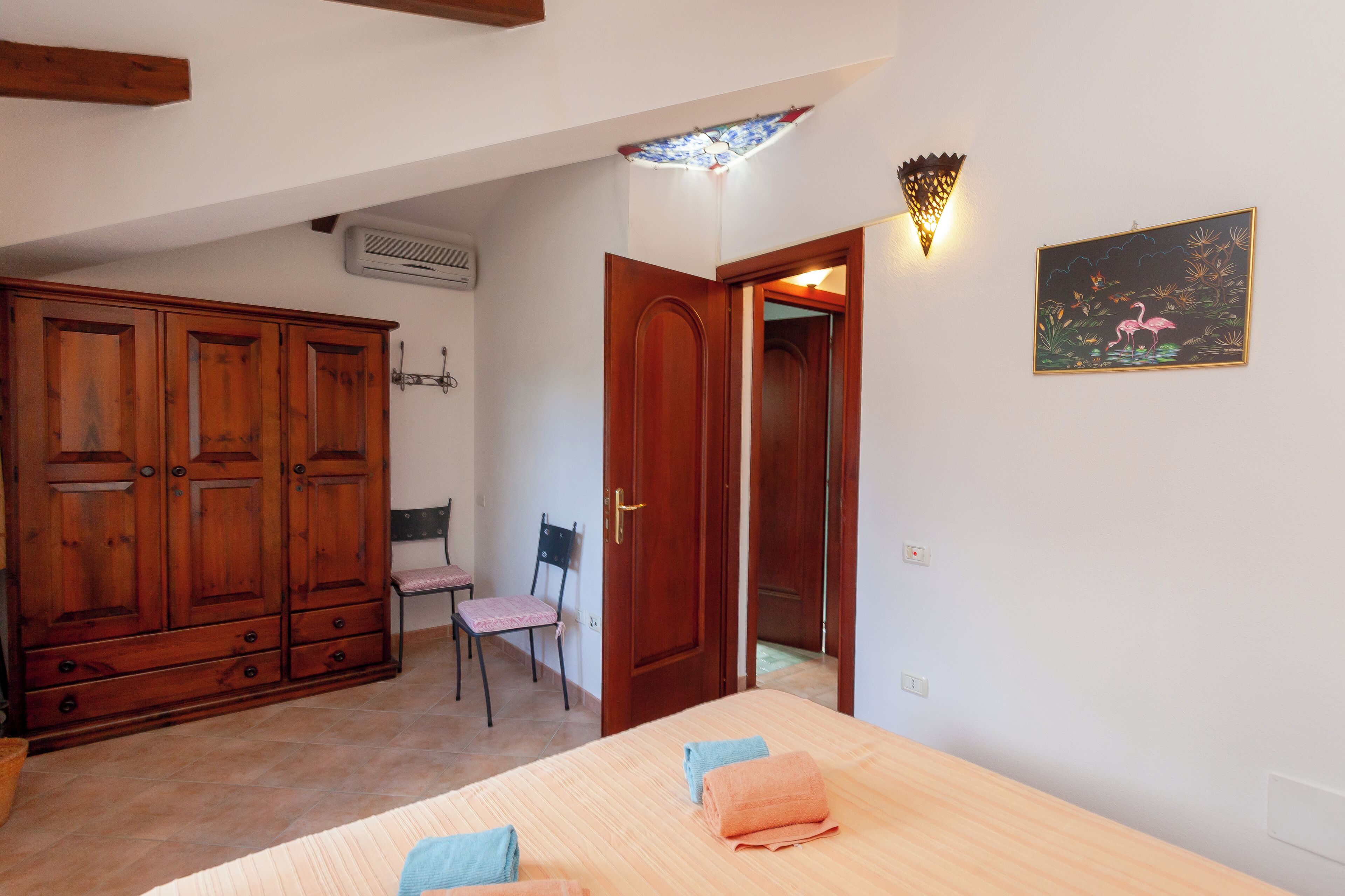 A bedroom with a bed, wooden wardrobe, and a chair.