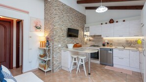 A compact kitchen with a stone accent wall, a TV, and a small dining area with stools.