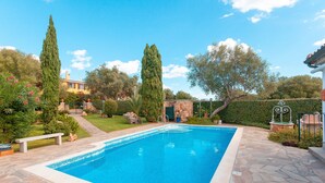 Una piscina rectangular con baldosas de piedra, rodeada por un jardín con árboles y un banco.
