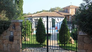 Una entrada portonada con muro de piedra y portón de metal, que conduce a un edificio con tejado de tejas y un letrero que dice "DOMAINE".