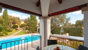 Un patio cubierto con piscina, mobiliario exterior y vistas al jardín y árboles circundantes.