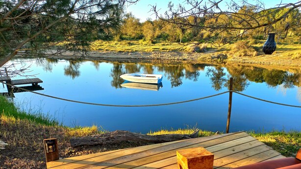 Eine Holzterrasse mit Seilgeländer, ein Boot auf dem Wasser und eine Vase am Ufer.