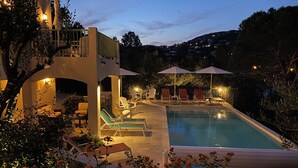 A pool area with lounge chairs and umbrellas, surrounded by greenery and a building with a balcony. - Air-conditioned villa, sea view and only 500m walk to sandy beach and San Peire! (Roquebrune-sur-Argens)