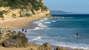 A beach with rocky outcrops, clear blue water, and a distant mountain range.