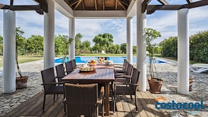 A covered outdoor dining area with a pool in the background.
