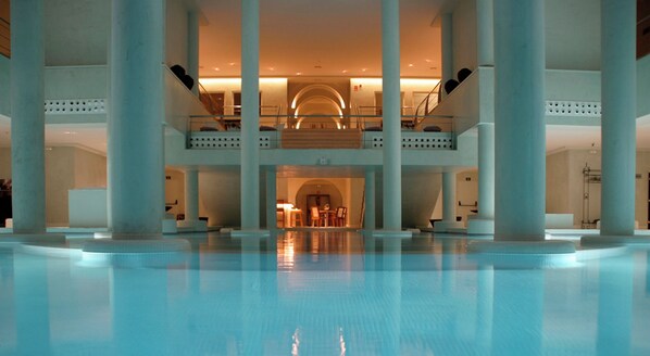 Un vaste espace intérieur abritant une piscine, avec un coin salon central et plusieurs niveaux de balcons.