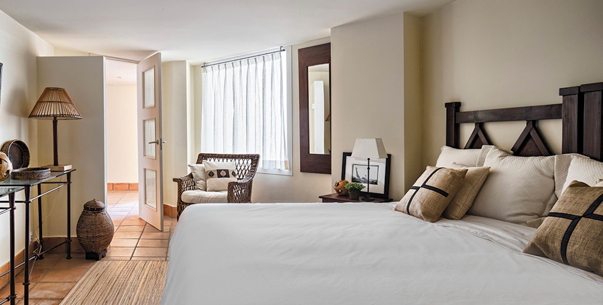 A hotel room with a large bed, a chair, a lamp, and a mirror.