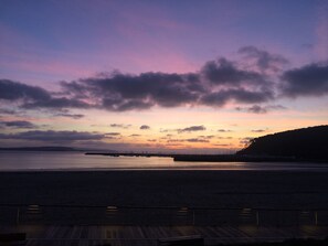 Un coucher de soleil sur une plage, avec une terrasse en bois au premier plan.