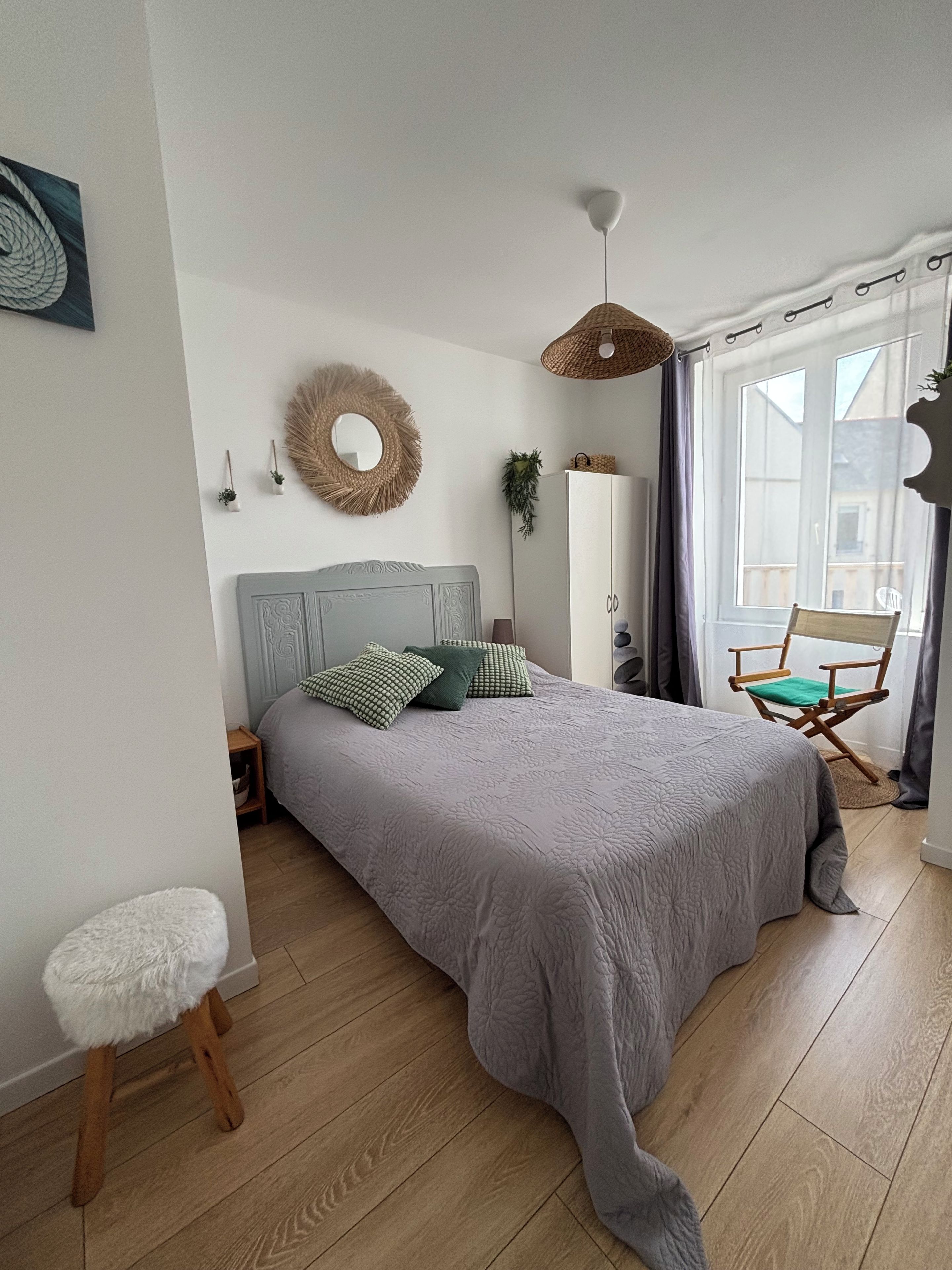 Une chambre à coucher comprenant un lit, une table de chevet, une chaise, une armoire, un miroir et une fenêtre.