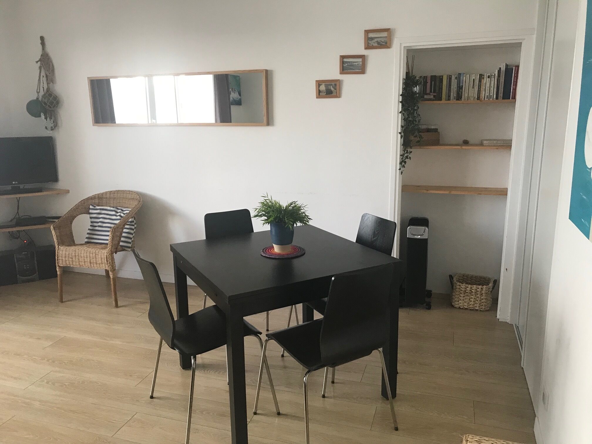 Un coin repas avec une table noire, quatre chaises, une plante en pot et une bibliothèque en arrière-plan.