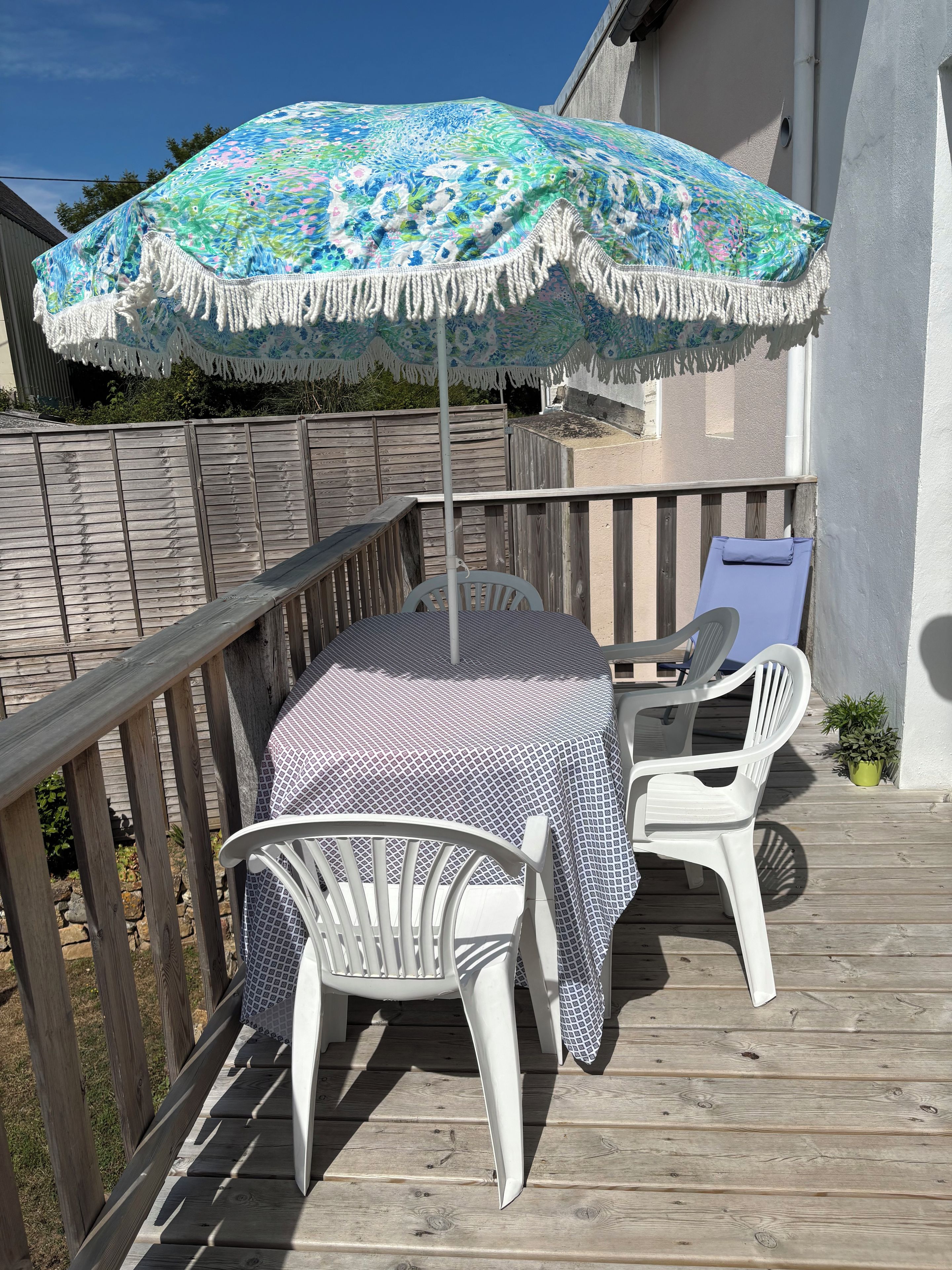 Une terrasse extérieure avec une table et deux chaises, un parasol à motifs et une clôture en bois.