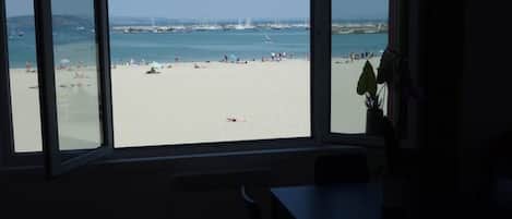 A room with a large window overlooking a beach with people and boats.