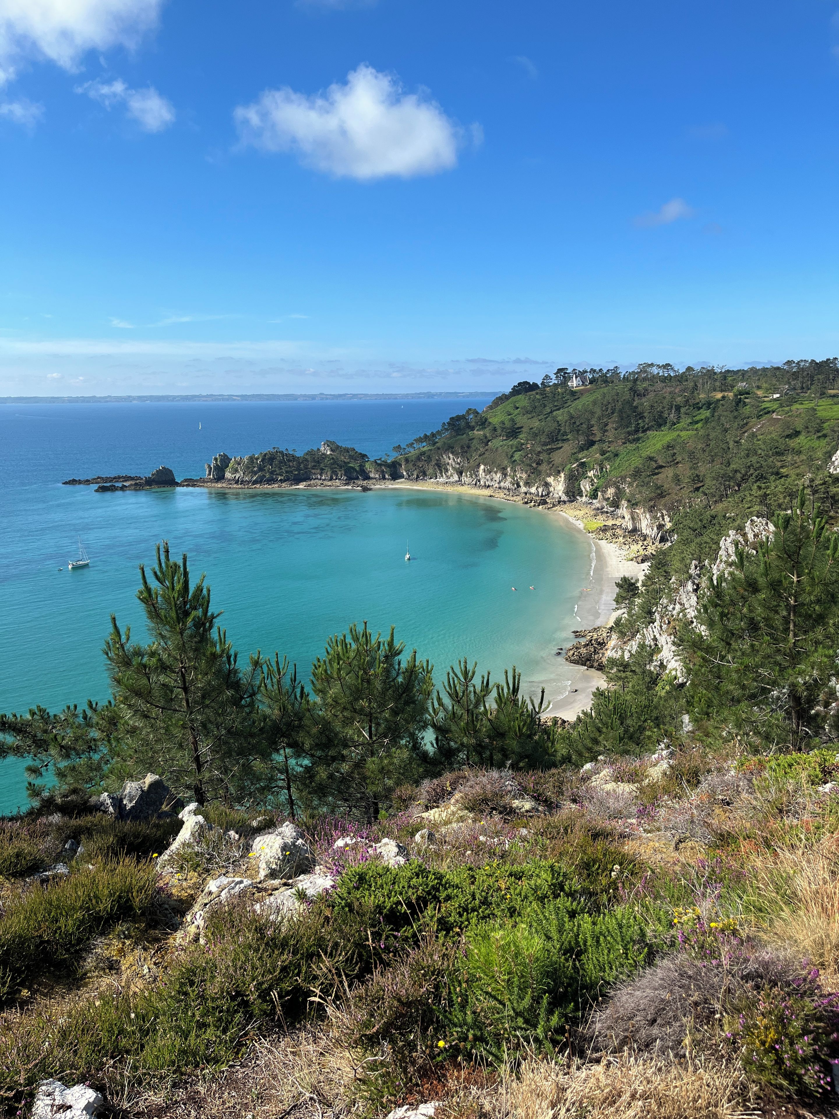 A coastal landscape with a clear view of the sea, a sandy beach, and a hilly terrain with vegetation.