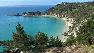 A coastal landscape with a clear view of the sea, a sandy beach, and a hilly terrain with vegetation.
