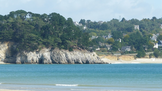 A coastal beach with a rocky cliff and houses in the background. - LE BIGORNEAU IMPRENABLE VIEW of the MORGAT CROZON BEACH (Crozon)