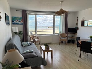 A living room with a sofa, chairs, a TV, and a view of the beach. - LE BIGORNEAU: UNBEATABLE VIEW of MORGAT CROZON BEACH, located just 50 meters away! (Crozon)