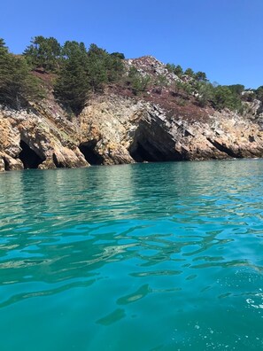 A coastal landscape with clear turquoise waters, rocky cliffs, and sparse vegetation.