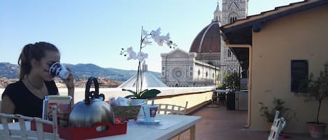A table with a teapot, a Coca-Cola bottle, and a basket of cornflakes. In the background, there is a building with a dome and a tower.