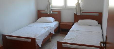 Una habitación pequeña y limpia con dos camas de madera, una mesita y una ventana con cortinas.