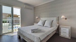 Ein Schlafzimmer mit einem Bett, zwei Nachttischen, einem Fenster und Blick auf einen Balkon.