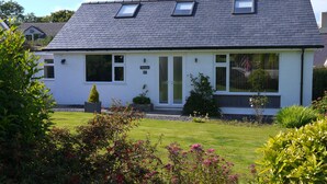 Ein eingeschossiges Haus mit Satteldach, einer kleinen Veranda und einem gepflegten Garten mit verschiedenen Pflanzen und Blumen.