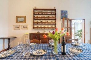 Une table à manger dressée avec une nappe bleue et blanche à motifs, des assiettes et des verres à vin, et un vase de tulipes placé au centre.