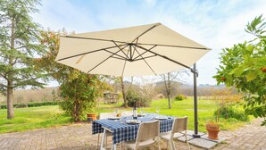 Un patio al aire libre con una mesa lista para comer, rodeada de sillas y una sombrilla que da sombra.