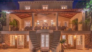 Une maison à deux étages avec une façade en pierre, un escalier central et des espaces de détente aménagés à l’extérieur.